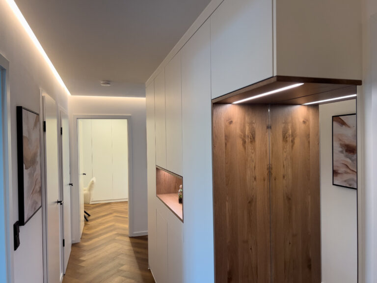 Flur mit indirekter LED-Beleuchtung in der Decken-Schattenfuge und integrierten Lichtleisten in einer Garderobennische.