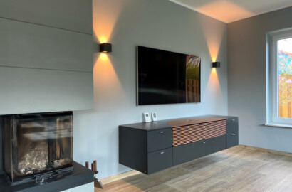 Wohnbereich mit moderner Up-&-Down-Wandleuchte, TV-Wand und Kamin