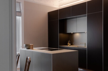 Moderne Küche mit Einbauspots in abgehängter Decke und indirekter Lichtführung über der Kücheninsel