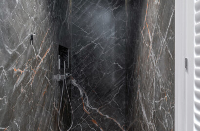 Walk-in-Dusche mit indirekter LED-Beleuchtung in der Schattenfuge und dunkler Natursteinverkleidung