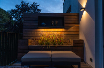 Balkon mit integrierter Holzbank, Pflanzwand und moderner Wandleuchte bei Nacht