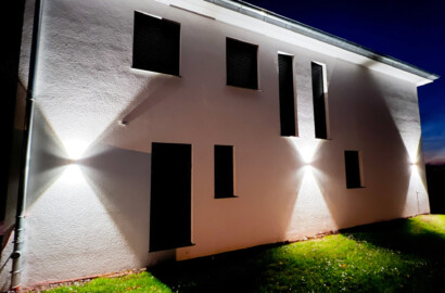Architektonische Außenwandleuchten mit Up-Down-Licht an moderner Hausfassade bei Nacht