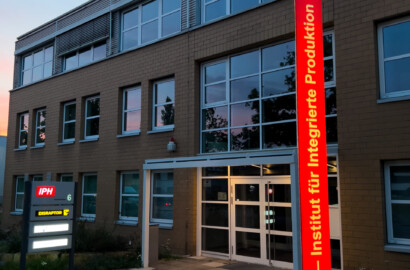 Illuminiertes Firmenschild mit roter Stele und akzentuierter Außenbeleuchtung am Institutsgebäude bei Dämmerung