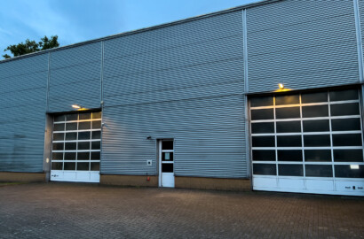 Industriehalle mit Metallfassade, großflächigen Sektionaltoren und funktionaler Außenbeleuchtung in der Dämmerung