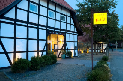 Außenansicht eines Fachwerkrestaurants mit beleuchteter Fassade und Leuchtschild in der Dämmerung