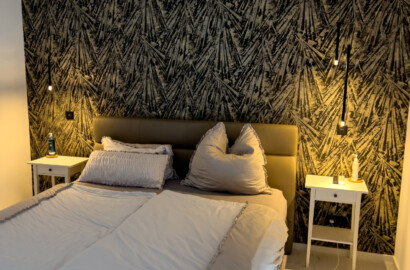 Pendelleuchten mit warmem Licht als elegante Nachttischbeleuchtung vor strukturierter Akzentwand im modernen Schlafzimmer
