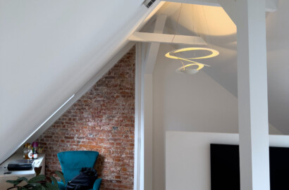Filigrane Pendelleuchte mit warmem, indirektem Licht in einem modernen Dachgeschoss mit sichtbaren Holzbalken