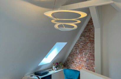 Skulpturale Pendelleuchte mit warmem, indirektem Licht als zentrales Interior-Element in einem wohnlichen Dachgeschoss