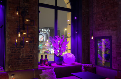 Akzentbeleuchtung in Restaurant mit indirektem Licht, violetter Lichtstimmung und beleuchtetem Fenster in Backsteinarchitektur