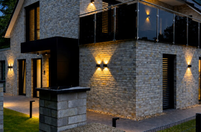 Moderne Fassadenbeleuchtung eines Einfamilienhauses bei Nacht mit Up-and-Down-Wandleuchten an einer Klinkerfassade.