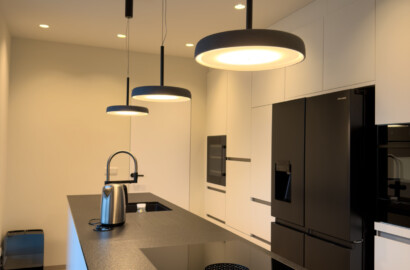 Moderne Küchenlichtplanung mit minimalistischen Pendelleuchten über einer Kochinsel, integrierten Einbauspots und harmonischer Beleuchtung in einer hochwertigen Designküche.