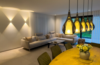 Moderne Wohnzimmer-Lichtplanung in einem offenen Wohn-Essbereich mit runden Up-and-Down-Wandleuchten hinter dem Sofa und einer Fünfer-Gruppe Pendelleuchten über dem Esstisch.
