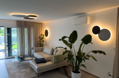 Modernes Wohnzimmer mit durchdachter Lichtplanung durch kreisförmige, indirekt leuchtende Wandleuchten und Deckenleuchten mit warmweißem Licht.