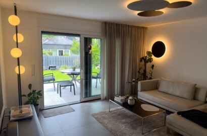 Modernes Wohnzimmer mit einer vertikalen Design-Stehleuchte mit runden Glaskugeln, einer indirekt beleuchteten Deckenrosette und einer runden Wandleuchte.