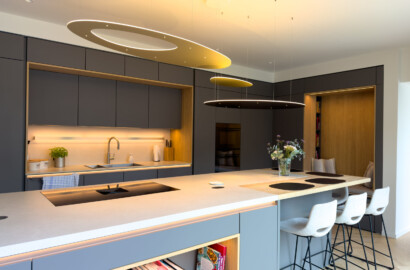 Moderne Kücheninsel mit Barhockern, integrierter LED-Schattenfugenbeleuchtung und organischen Pendelleuchten.