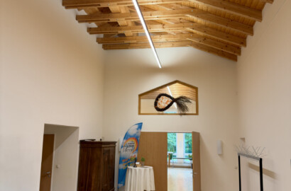 Hoher Foyerbereich mit Holzdachstuhl und einer langen LED-Linearleuchte, die den Weg in den Saal führt
